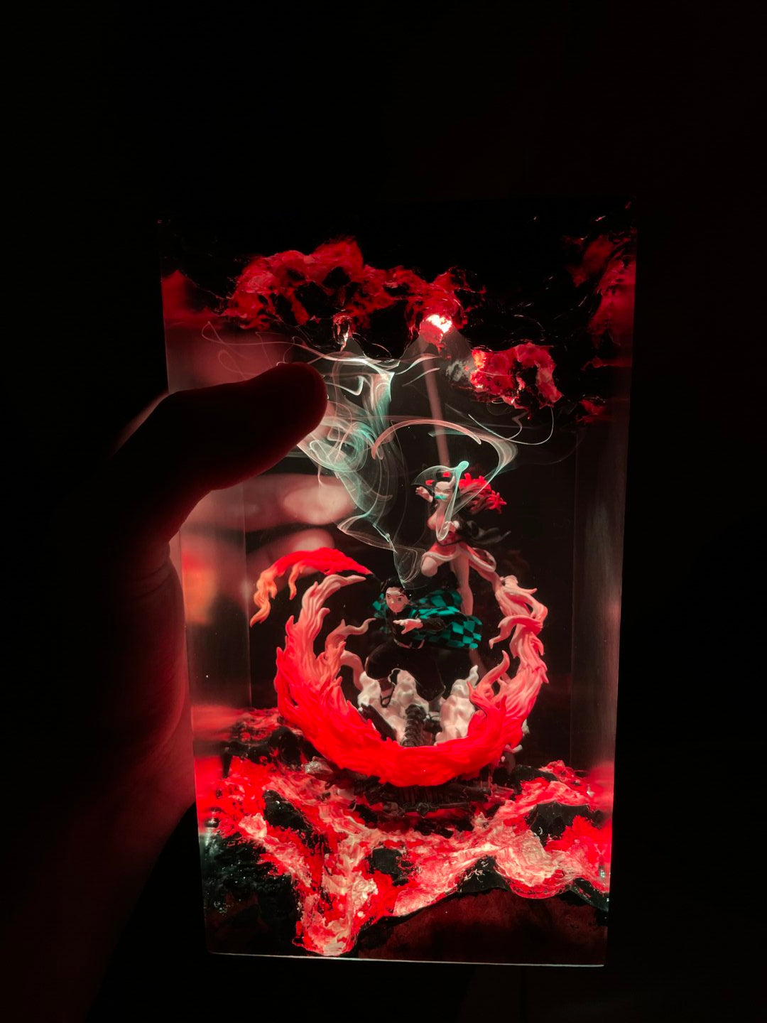 Close-up of a hand holding a transparent object with red and green smoke effects on a dark background